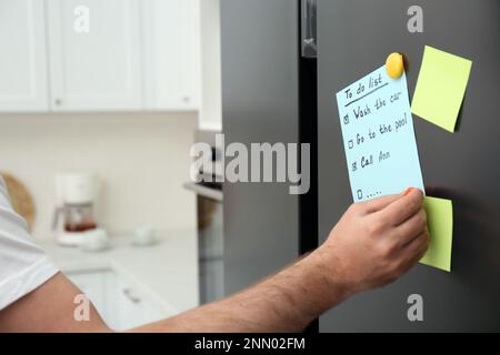 Homme mettant à faire la liste sur la porte du réfrigérateur dans la cuisine, fermé Banque D'Images