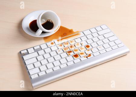 Tasse de café renversée sur le clavier de l'ordinateur sur une table en bois Banque D'Images