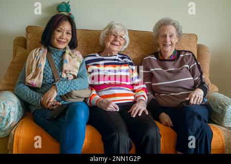 Deux femmes anglaises très âgées dans leurs 90s s'assoient sur un canapé avec une femme vietnamienne d'âge moyen. Banque D'Images