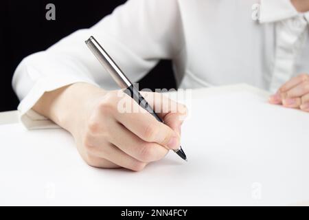 Une jeune main féminine écrira quelque chose sur une feuille de papier vierge Banque D'Images