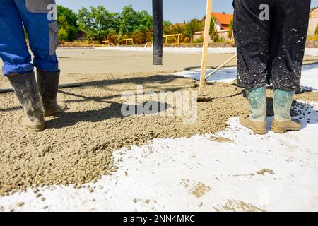 Le travailleur de la construction dirige le tube de pompe dans la bonne direction, versant une couche de béton dans la fondation de bâtiment couvrant le renforcement carré, ano Banque D'Images