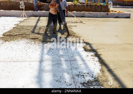 Le travailleur de la construction dirige le tube de pompe dans la bonne direction, versant une couche de béton dans la fondation de bâtiment couvrant le renforcement carré, ano Banque D'Images