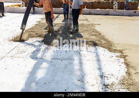 Le travailleur de la construction dirige le tube de pompe dans la bonne direction, versant une couche de béton dans la fondation de bâtiment couvrant le renforcement carré, ano Banque D'Images