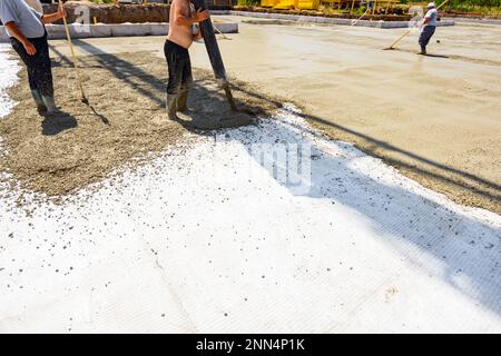 Le travailleur de la construction dirige le tube de pompe dans la bonne direction, versant une couche de béton dans la fondation de bâtiment couvrant le renforcement carré, ano Banque D'Images