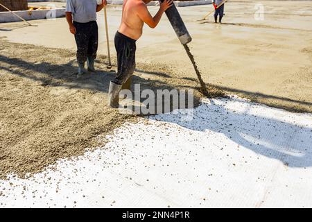 Le travailleur de la construction dirige le tube de pompe dans la bonne direction, versant une couche de béton dans la fondation de bâtiment couvrant le renforcement carré, ano Banque D'Images