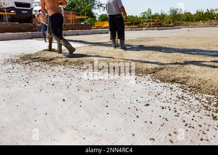 Le travailleur de la construction dirige le tube de pompe dans la bonne direction, versant une couche de béton dans la fondation de bâtiment couvrant le renforcement carré, ano Banque D'Images