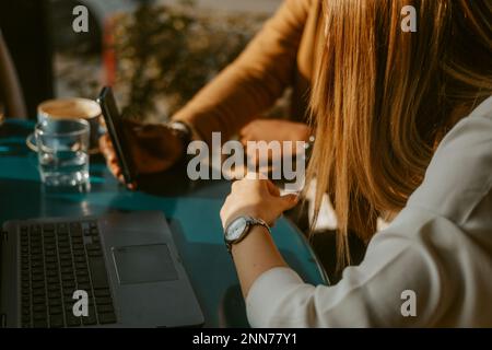Gros plan de deux personnes en voyage d'affaires regardant le téléphone tout en étant assis au café Banque D'Images