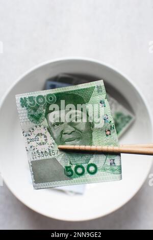 Manger de l'argent avec des baguettes, manger des notes nigérianes 500 Naira avec des baguettes Banque D'Images