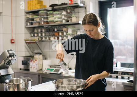 Une femme cuisinière travaille dans une cuisine industrielle moderne. Le processus de fabrication de gâteaux dans une boulangerie ou un café. Banque D'Images