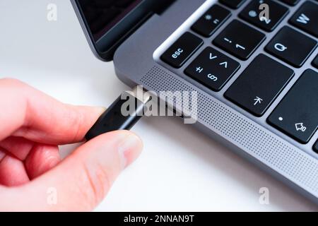 Illustration du processus de connexion de périphériques à un ordinateur portable : branchement manuel d'un câble USB de type C dans le port d'un ordinateur portable. Présentation de la commodité de la moder Banque D'Images