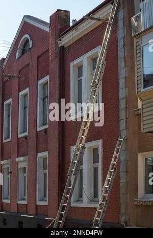 Une échelle d'extension s'appuie contre l'avant d'un bâtiment de logement multifamilial pour préparer les réparations de toit. Banque D'Images