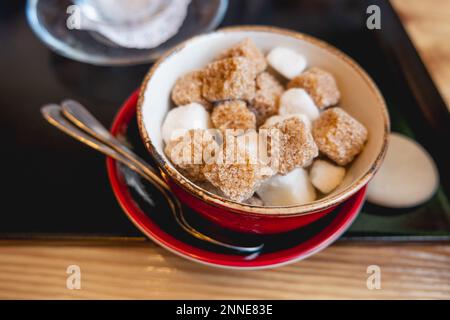 Bol rouge avec deux types de sucre - le sucre blanc et le sucre de canne. Des cubes sucrés pour une boisson chaude au café. Banque D'Images