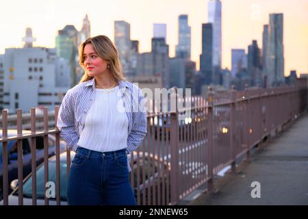 Une jeune femme blonde vêtue de vêtements décontractés, debout sur le pont de Brooklyn dans la ville de New York, regardant sur le côté Banque D'Images