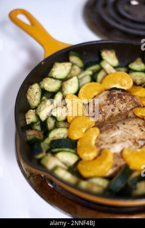 Gros plan des cuisses de poulet cuites au four dans une casserole en fonte jaune, cuite avec des épices, des courgettes et des oranges mandarines. Banque D'Images