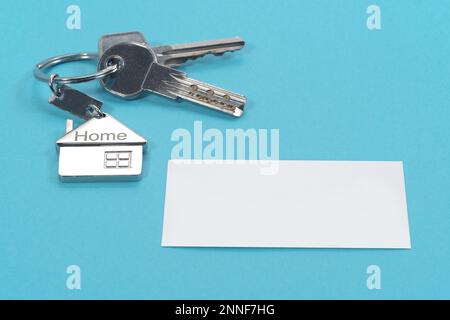 Symbole maison avec touches argentées et carte de visite blanche vierge sur fond bleu. Concept immobilier Banque D'Images