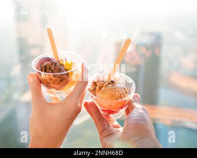Homme et femme tient des bols en plastique avec des boules colorées de glace. Dessert froid pour les journées ensoleillées. Différentes glaces avec des cuillères. Une date romantique au café. Banque D'Images