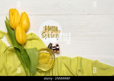 Carte avec texte HELLO SPRING, fleurs de tulipe, bouteille de parfum et vêtements sur fond de bois clair, gros plan Banque D'Images