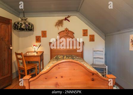 Ancien lit simple avec tête de lit et repose-pied en bois, bureau avec service de notaire et siège à bascule en cuir brut tissé dans la chambre à l'étage. Banque D'Images