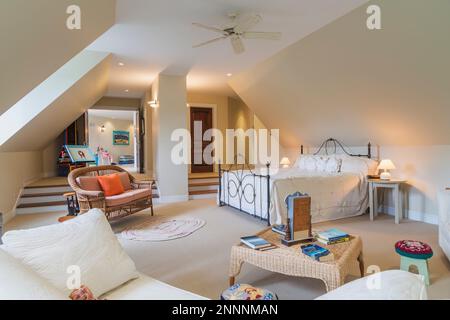 Très grand lit avec tête de lit en fer forgé de style ancien et repose-pied avec canapés en osier et tissus blancs, table basse dans la chambre principale recouverte de moquette. Banque D'Images