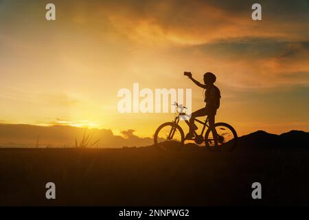 Silhouette de femme à vélo au coucher du soleil, gaiement à la fin de la journée. Femme à cheval pause se détendre et prendre une photo paysage et regarder avant guerre Banque D'Images