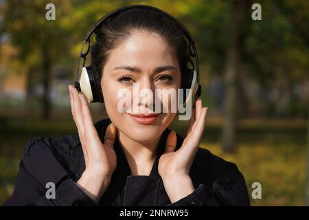 Jeune femme d'une 20s Écoutez de la musique avec des écouteurs sans fil sur l'extérieur, dans la nature sur une journée ensoleillée Banque D'Images