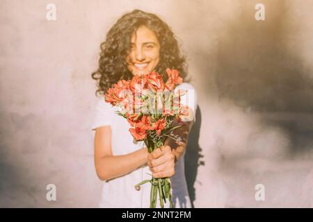 jeune femme debout contre le mur tenant (alstroemeria) les mains de bouquet de fleurs rouges Banque D'Images