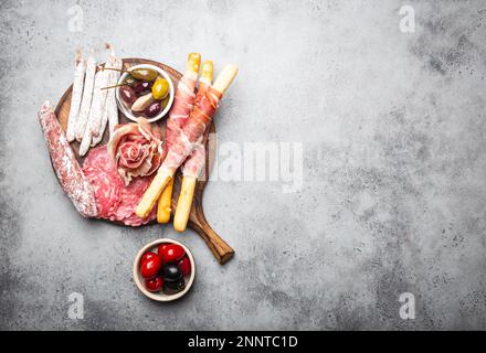 Variété de viandes froides et hors-d'œuvre, prosciutto, jamon, tranches de salami, saucisse, grissini, olives. Assortiment de viandes sur bois rustique Banque D'Images