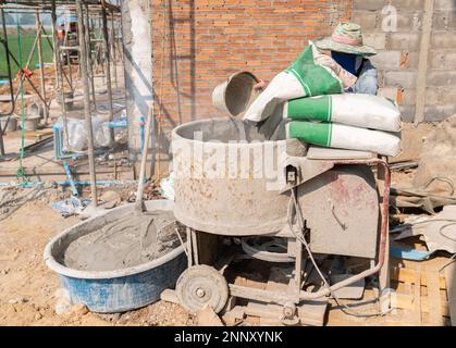 Builder travaillant avec un seau dans ses mains charge un mélangeur de béton.orange mélangeur de béton prépare le mortier de ciment Banque D'Images