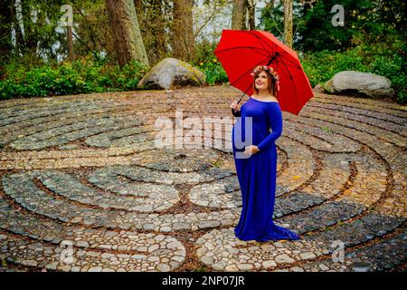 Femmes enceintes en robe bleue devant un labyrinthe de pierre avec parapluie rouge Banque D'Images