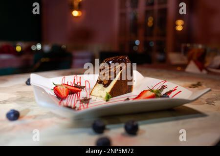 dans un café, pongez le gâteau avec du chocolat et des baies sur une assiette. Banque D'Images