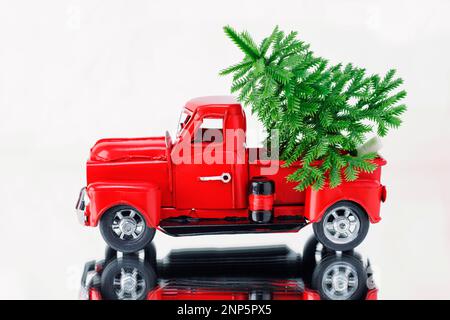 Arbre de Noël dans un camion de Noël rouge sur fond blanc, reflété dans une surface miroir. Concept - carte de vœux pour Noël et nouvel an, holi Banque D'Images