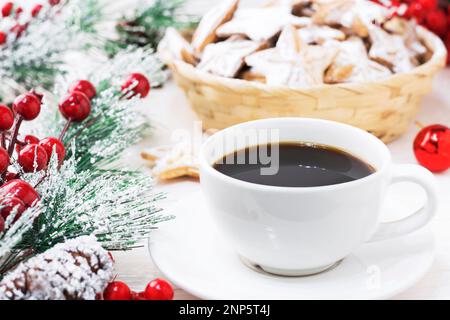 Une tasse blanche de café Americano noir sur fond blanc en bois à côté de la branche de noël et des biscuits , et les jouets du nouvel an. Noël, nouvel an Banque D'Images