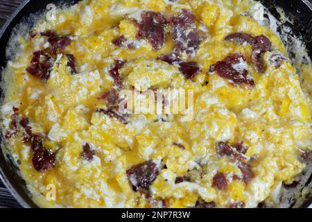 Œufs brouillés avec pastrami, plat à base d'œufs remués, fouettés ou battus ensemble tout en étant légèrement chauffé, avec sel, beurre, huile et PE noir Banque D'Images