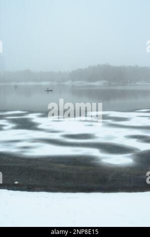 Flou et bruit dans une tempête de neige sur la première glace du lac c pêcheurs sur les bateaux devant les bâtiments dans le brouillard. Banque D'Images