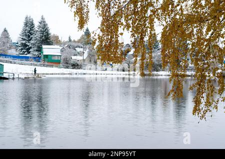 Le pêcheur à la ligne moderne dans un costume de protection bleu se dresse sur les rives enneigées des birches de montagne dans la neige au bord de l'eau du lac pour tourner la Russie Banque D'Images