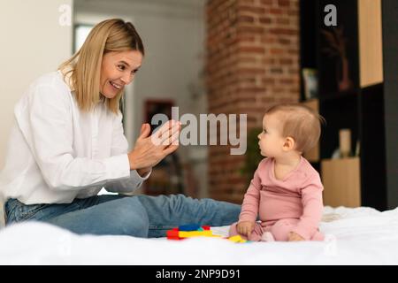 Une mère heureuse souriant et jouant main de clap avec son adorable petite fille, assise sur le lit à la maison Banque D'Images