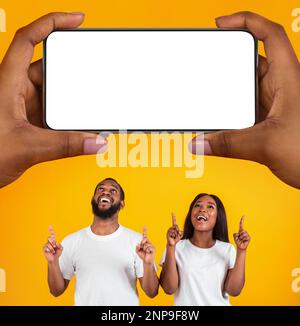 Joyeux couple noir pointant vers le smartphone Big Blank dans les mains des femmes géantes Banque D'Images