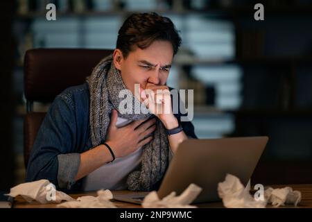 Un employé malsain travaillant tard au bureau, toussant Banque D'Images