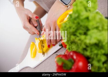 l'adulte enseigne à l'enfant de couper des légumes la mère aide son à couper le poivron jaune les mains en gros couteau porcelaine tableau blanc les légumes sains les premières étapes de la formation à la cuisine Banque D'Images