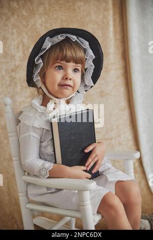 Portrait rétro d'un bel enfant dans un fauteuil à bascule avec livre Banque D'Images