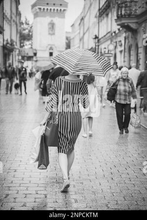 Femme mince dans une robe rayée marche avec parapluie rayé à Varsovie Banque D'Images