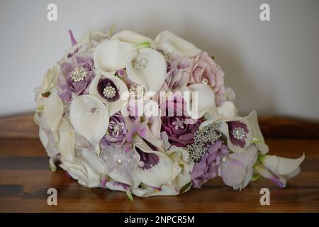 Bouquet de mariage en cascade avec nénuphars, roses violettes, décoré de bijoux en argent, de perles et de soie posé sur une table en bois Banque D'Images