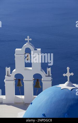 Vue sur une église traditionnelle en dôme bleu et clocher blanc avec la mer et la caldeira au-delà. Banque D'Images