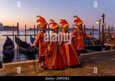 Les amateurs de carnaval vêtus de magnifiques costumes de couleur orange pendant le carnaval de Venise 2023 tôt le matin sur la place Saint-Marc, Venise, Italie en février Banque D'Images