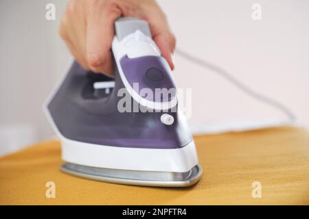Une personne repassant du tissu jaune avec un fer à repasser. Gros plan. Banque D'Images