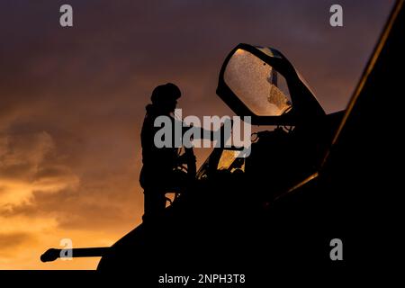 Le pilote de chasse monte à bord de son intercepteur de chasseur à réaction pour une mission d'entraînement au combat au coucher du soleil. Silhouette dramatique de pilote de héros se préparant à la guerre Banque D'Images