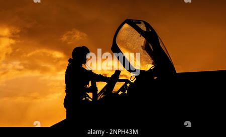 Le pilote de chasse monte à bord de son intercepteur de chasseur à réaction pour une mission d'entraînement au combat au coucher du soleil. Silhouette dramatique de pilote de héros se préparant à la guerre Banque D'Images