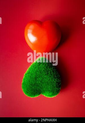 Herbe verte et balle de coeur rouge isolée sur fond rouge, style vertical. Amour, don. Environnement et protection durable, écologique, amour Banque D'Images