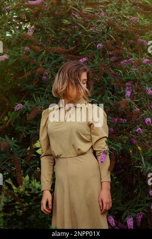 Bonne femme dans la bourddleia fleurs champ dans la luxueuse robe d'or.Jeune femme en robe d'or debout dans le champ de fleurs. Banque D'Images