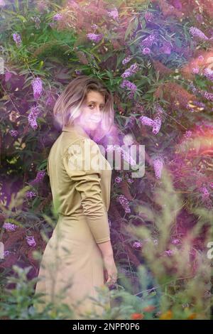 Femme émotive s'amusant à l'extérieur près des fleurs de la Buddleia. Portrait d'une belle blonde sur le coucher de soleil dans la nature. Banque D'Images